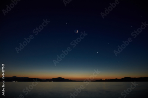 Young crescent Moon with stars and planets over ocean sea waters.