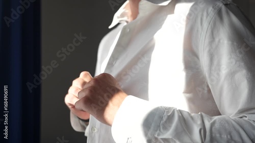 Man buttoning white shirt close up with natural light