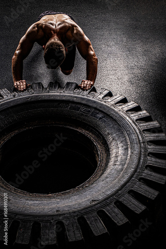 A man with a handsome body pushes a huge wheel. The muscles of the shoulders and back are clearly visible.