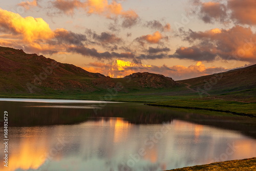 View of placid lake mirroring the fiery sunset and rugged mountains, a serene landscape painting of nature's grandeur, Deosai National Park, Gilgit Baltistan, Pakistan.
