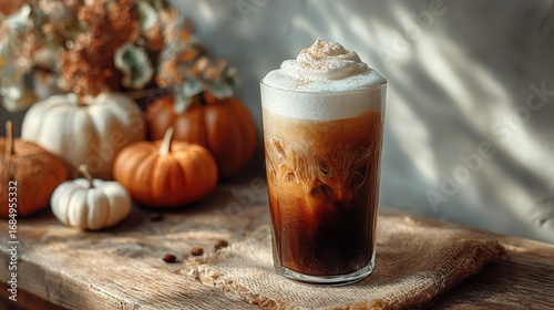 A tall glass of iced coffee topped with creamy pumpkin cold foam on a rustic wooden table with soft autumn sunlight filtering through a window cozy seasonal beverage concept