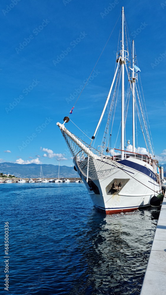 Fototapeta premium A white boat with sails docked in a harbor on a sunny day with a clear blue sky
