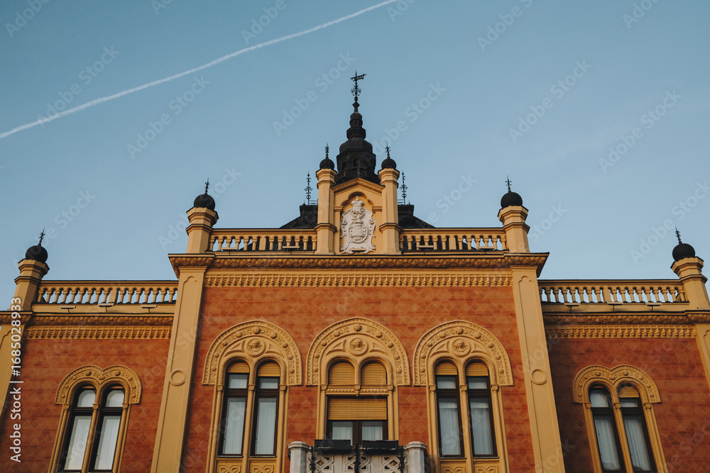 Fototapeta premium Ornate yellow orange facade of a historic building in Novi Sad, Serbia, captured in winter sunset light