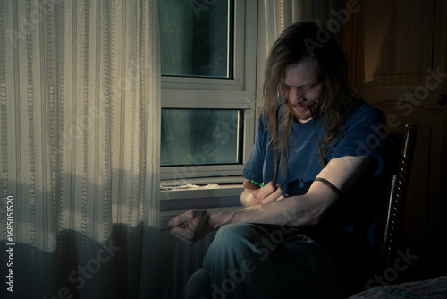 The High and The Low. A drug user injecting his arm with a syringe in a darkened room. The image conveys the difficult issues of drug addiction and abuse.