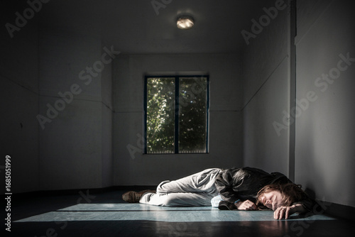 The High and The Low. A man lying on the floor in a dimly lit hallway. The image captures the loneliness, isolation, and desperation of drug addiction and homelessness.