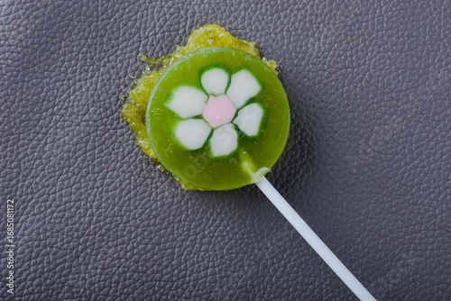  A green sticky lollipop, a dip on the upholstery of a gray leather sofa. Concept of daily stains and routine cleaning. Spot-cleaning upholstery or carpets. top view