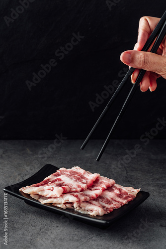 Fotografie Sliced Raw Meat on Plate with Chopsticks Against Dark Background