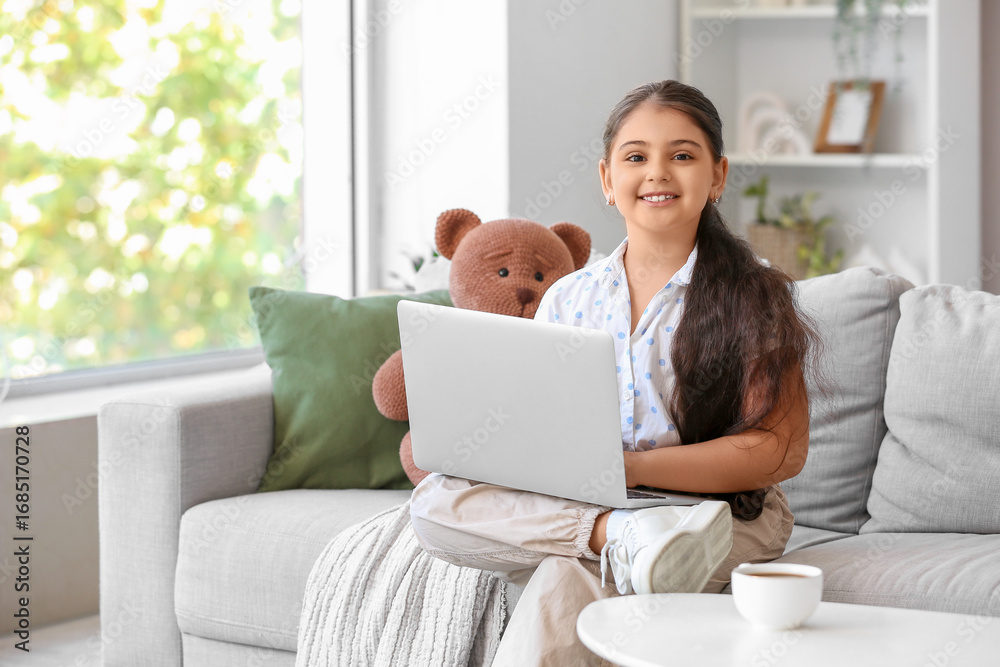 Fototapeta premium Little girl using laptop on sofa at home