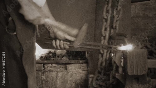 Vintage Blacksmith Forging Hot Iron Chain Links in Workshop.
Sepia-toned footage of a traditional blacksmith hammering heated iron to forge a chain link.