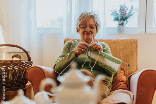 Konstfotografi A cheerful senior woman enjoying knitting while seated in a cozy living room, expressing creativity and relaxation