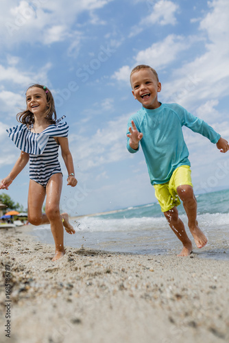 Картината върху платно Children play joyfully on the beach while splashing in the water under a partly