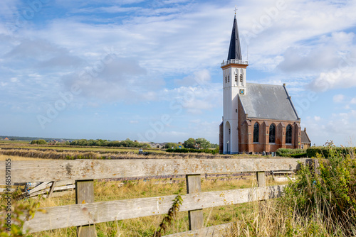 Typical landscape of Texel island with small village and picturesque church (Hervormde kerk) under blue sky and white clouds, A little town on the wadden islands, Den Hoorn, Noord Holland, Netherlands