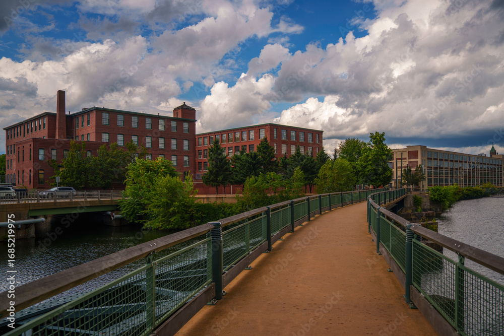 Naklejka premium Lowell’s industrial historic district in Massachusetts features landmark mill buildings rising above canal waterways fed by the Merrimack River, preserving the legacy of America’s textile revolution.