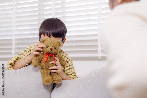 Asian boy using teddy bear to express emotions during psychological counseling session in ADHD therapy showing attachment and reflective behavior in mental health support environment