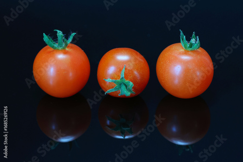 Three tomatoes on a dark reflective surface