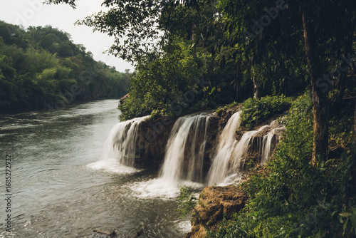 Sai Yok Yai waterfall flowing into the river Kwai surrounded by lush vegetation, creating a serene natural landscape in Kanchanaburi, Thailand