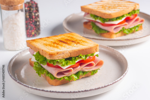 Close-up of two sandwiches with bacon, salami, prosciutto and fresh vegetables on rustic wooden cutting board. Club sandwich concept