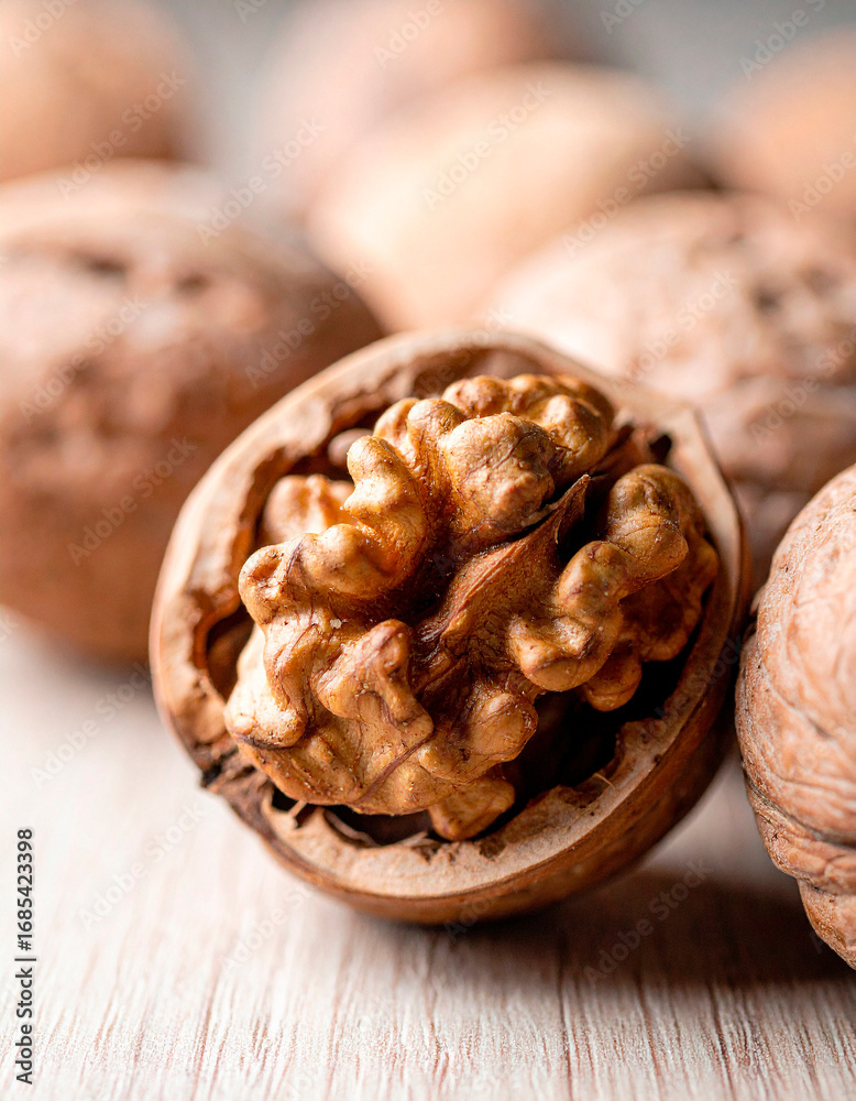 Fototapeta premium Walnuts with shells and a focus on a single opened nut on a wooden surface, showcasing their rich texture and natural color