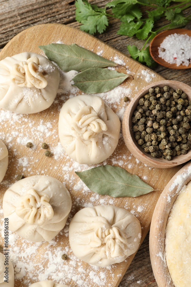 Fototapeta premium Uncooked khinkalis (dumplings) with peppercorns, flour, parsley and bay leaves on wooden table, flat lay