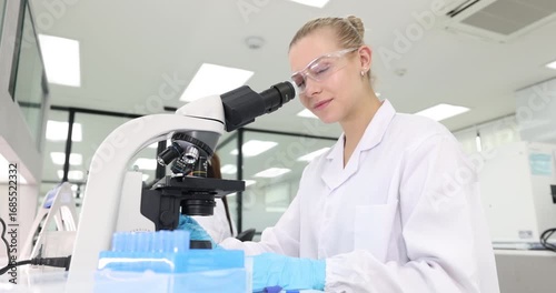 A female scientist carefully examines samples under a microscope before turning her face and smile to camera