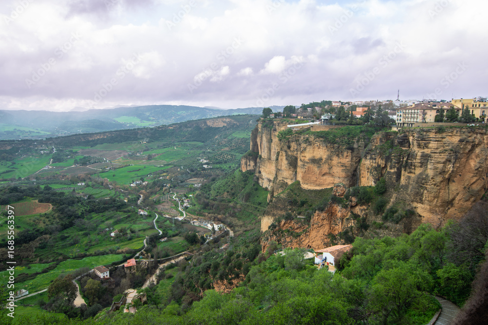 Fototapeta premium Wide angle panoramic view of the clifftop town of Ronda Spain showing the dramatic precipice and the lush green valley below after a rainfall in springtime.