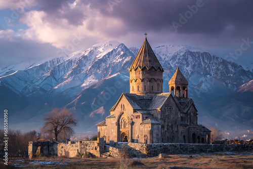 Ancient Armenian church in Yeghegis illuminated by sunset against snowy mountains.