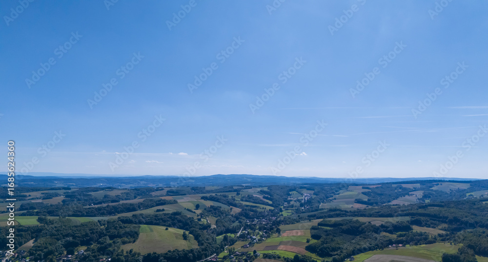 Fototapeta premium A panoramic view of rolling green hills under a clear blue sky, capturing the serene beauty of the countryside landscape. Ideal for nature and travel themes.