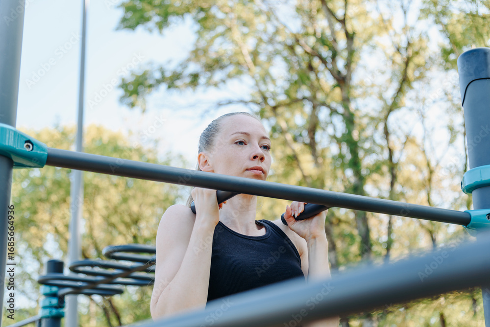 Obraz premium young sportive caucasian woman doing exercises on horizontal bar outdoors in summer, beautiful redhead girl, black sportswear, healthy lifestyle concept