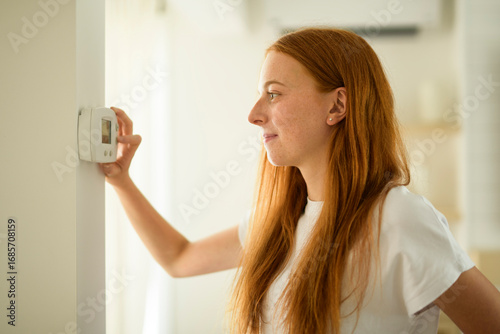 Fotografia Smiling woman standing near wall-mounted device adjusting degrees in living room