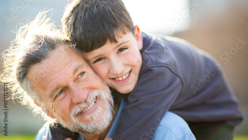 Grandfather and boy smiling closely in warm sunlight hug