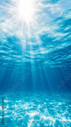 Underwater view of sun rays streaming through clear blue water illuminating sandy ocean floor