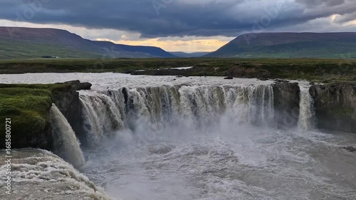 Front view of Goðafoss waterfall in Iceland with powerful water flow and dramatic sunset-lit clouds in the sky