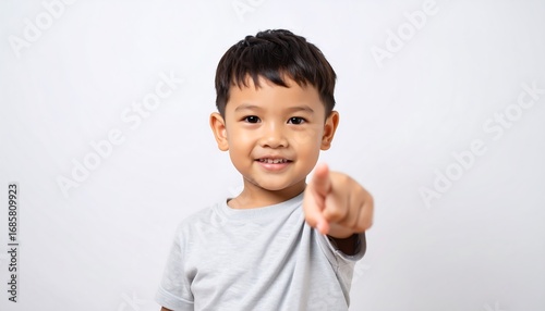 A cheerful little boy points directly at the camera, standing against a plain white background