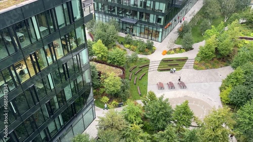 Urban garden at a modern office campus biophilic courtyard, glass facades, amphitheater benches, walkable paths showcasing green architecture, sustainability and smart-city design for community wellb