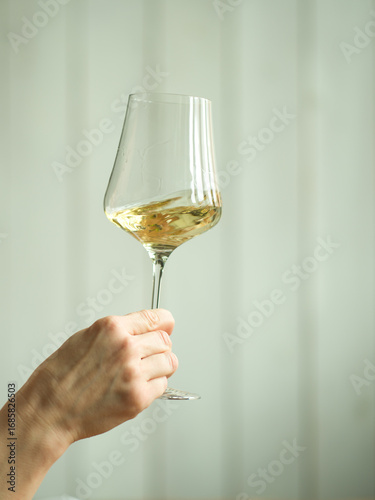 hand swirling a glass of white wine against white wooden wall