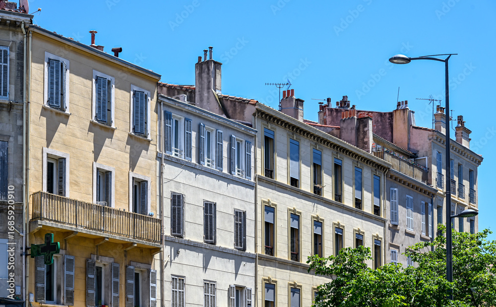 Obraz premium Row of classic apartment buildings, blue sky and pharmacy sign, rue de Lodi, Marseille, Mediterranean cityscape, Provence, France, rue de Lodi, Marseille