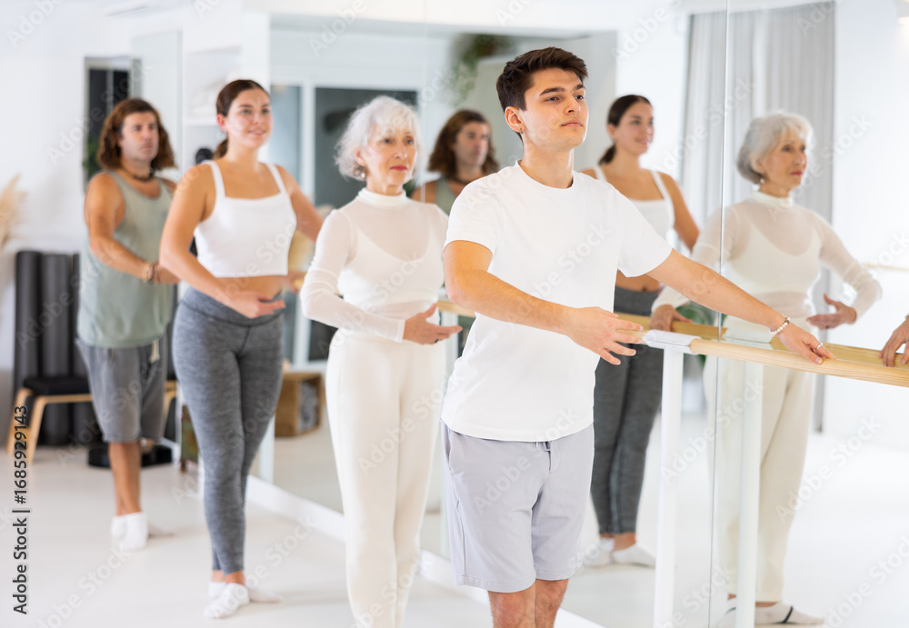 Fototapeta premium Slender young man practicing ballet at ballet barre in gym room during training session