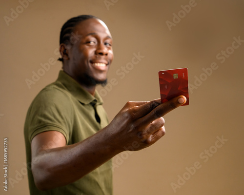 Quadro su tela Smiling Nigerian man in a green shirt holding a debit card towards the camera, shot from a side angle in a studio setting