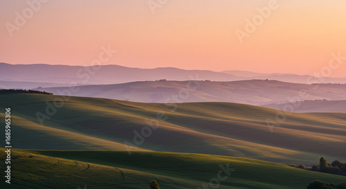 Serene rolling green hills bathed in soft golden light at sunset with layered purple mountains background.