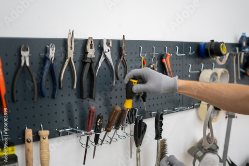 Wallpaper Mural In a workshop setting, a person in gloves carefully selects a tool from a neatly organized pegboard, highlighting focus and preparation for a task ahead. Torontodigital.ca