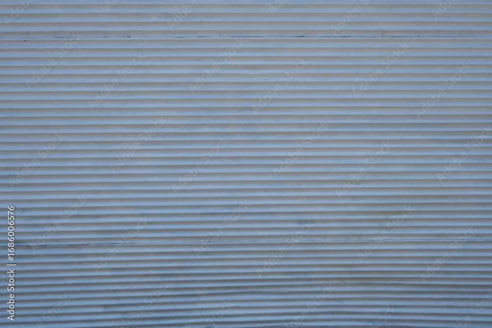 Fototapeta premium White metallic rolling door backdrop. White metal shutter background. Closed shop shutter surface texture. Steel roller shutter pattern.