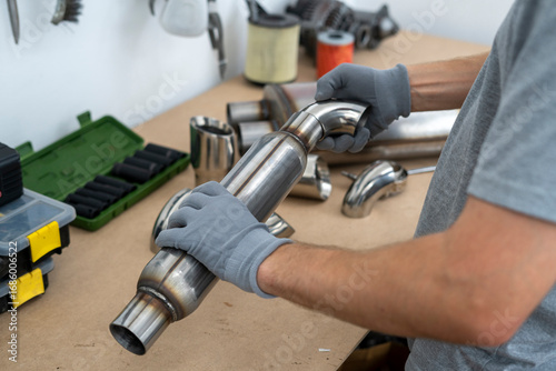 Wallpaper Mural A person is handling a metal exhaust component while surrounded by various pipes and tools, preparing for installation in a workshop setting. Torontodigital.ca