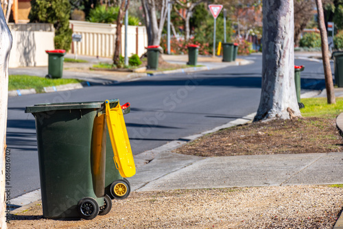 Household wheelie bin with a yellow recycling lid placed on the curb of a suburban street in Melbourne, Australia, with more bins lined up along the road. Concept of waste management, recycling system