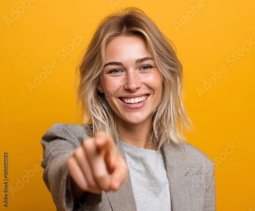 A joyful woman with a warm smile directs her finger directly at the viewer against a bright yellow backdrop.