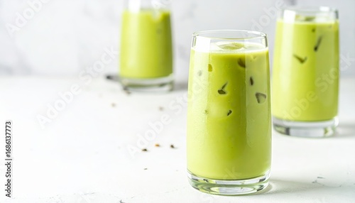 Green matcha tea mixed with ice cube and milk in latte glass on white