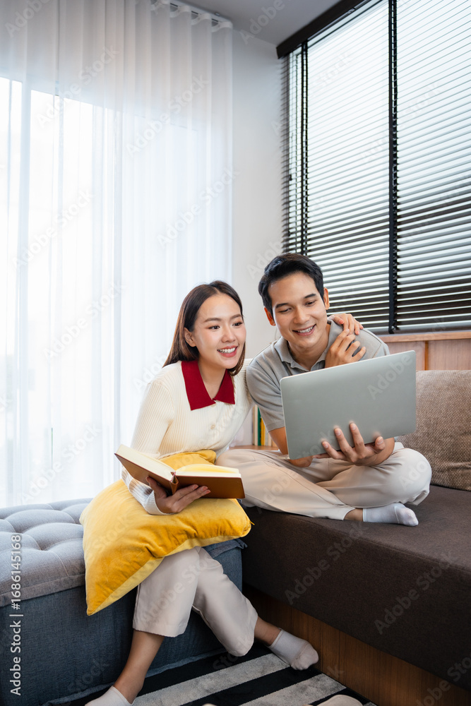Fototapeta premium happy young couple relaxing together on the sofa at home and reading book and using laptop computer . couple having a conversation together while relaxing on the couch. Copy space.
