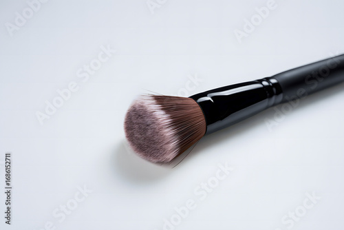 Elegant makeup brush with a black handle and soft, light-colored bristles against a subtle, abstract background