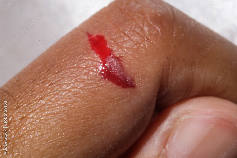 Fototapeta premium Close-up shot of a brown-skinned man's bleeding index finger. Injured finger due to workplace accident. Blood flowing motion. Health care and medicine. Human body parts in macrophotography
