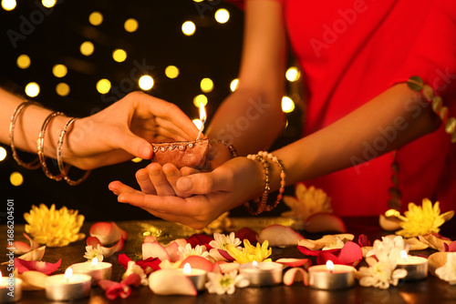 Women holding beautiful diya lamp for Diwali with candles, flowers and petals on dark blurred background