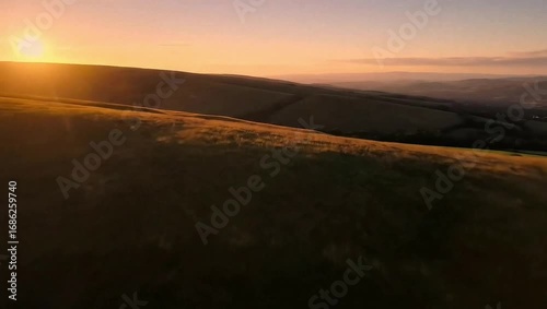 Golden hour sunset over rolling hills and grassy fields with distant hazy landscape